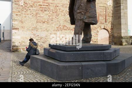 16. Februar 2021, Rheinland-Pfalz, Trier: Eine Frau sitzt auf dem Sockel der Karl-Marx-Statue am Simeonstiftplatz. Die Statue wurde am 5. Mai 2018 anlässlich des 200th. Jahrestages der Geburt von Karl Marx in seiner Heimatstadt enthüllt. Der Philosoph, Ökonom, Journalist und Autor des "Kapitals", der Kritik der kapitalistischen Gesellschaft des 19th. Jahrhunderts, wurde am 5. Mai 1818 in Trier geboren. Foto: Andreas Arnold/dpa Stockfoto