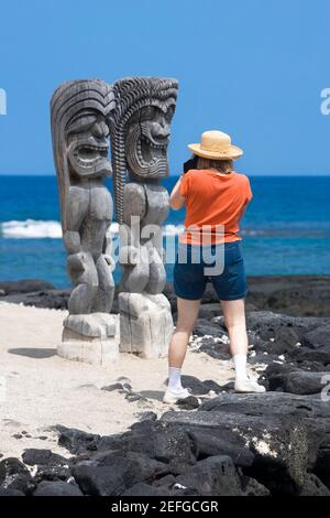 Rückansicht einer Frau, die ein Foto von Tikies an der Küste macht, Puuhonua O Honaunau National Historical Park, Kona Coast, Big Island, Hawaii Islands, USA Stockfoto