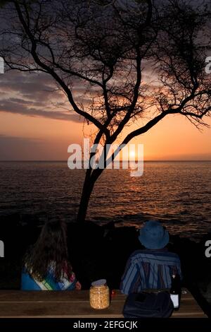 Mann und Frau, die den Sonnenuntergang über dem Meer betrachten, Pakini Nui Wind Project, South Point, Big Island, Hawaii Islands, USA Stockfoto