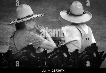 Ein Seniorenpaar mit Western Vaquero und Sonnenhüten entspannen sich auf einer Parkbank in Santa Fe, New Mexico. Stockfoto