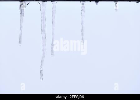 Nahaufnahme von schmelzenden Eiszapfen, die von einem Dach am hellgrauen Himmel hängen. Gesehen in Deutschland im Februar Stockfoto