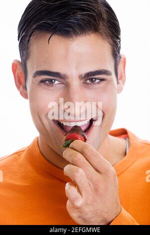 Porträt eines mittleren Erwachsenen Mann essen eine Schokolade getaucht Erdbeere Stockfoto