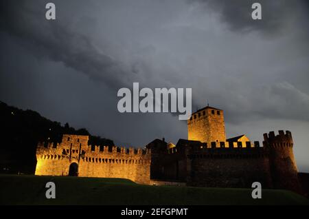 Beleuchtete Burg Castelgrande bei Nacht mit Sturmwolken und Blitz in Bellinzona, Schweiz. Stockfoto