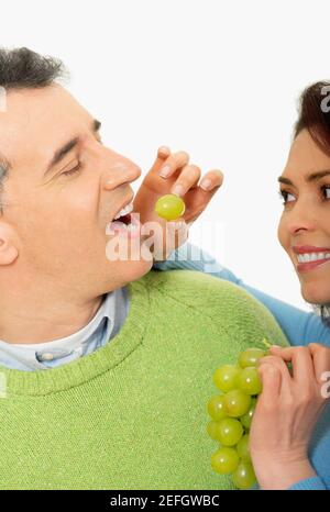Nahaufnahme einer mittleren erwachsenen Frau, die eine Traube füttert Ein mittelerwachsener Mann Stockfoto