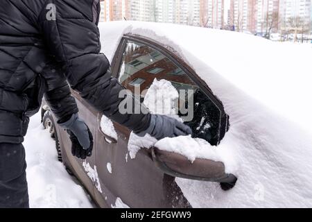 Ein Mann räumt Schnee aus seinem Autofenster. Auto im Schnee nach einer Nacht Schneesturm Stockfoto