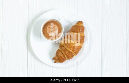 Ein Croissant und eine Tasse Kaffee aus Kunstschaum auf Weiß Blick von oben auf den Holztisch Stockfoto