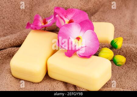 Gelbe Seifen und Orchideenblüten auf braun Handtuch. Stockfoto