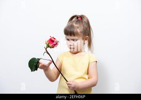 Kind Mädchen in einer gelben Bluse hält eine verdorrte Rose In ihren Händen und ist nicht glücklich Stockfoto