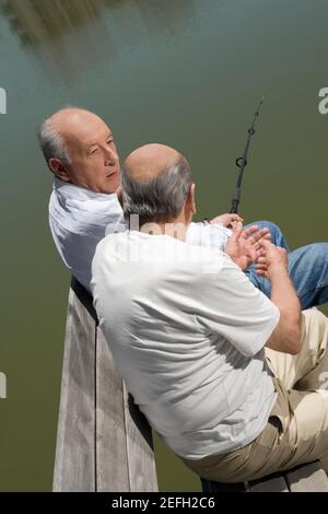 Blick auf zwei ältere Männer, die auf einem sitzen Bank am See und Angeln Stockfoto