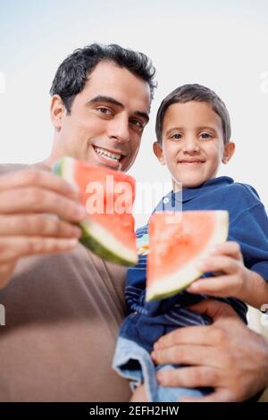 Porträt eines mittleren Erwachsenen Mann trägt seinen Sohn und Halten Sie Scheiben von Wassermelone Stockfoto