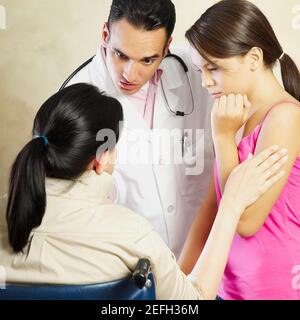 Ein Arzt spricht mit einer Patientin, die in einem Rollstuhl sitzt und ihre Tochter neben ihr steht Stockfoto