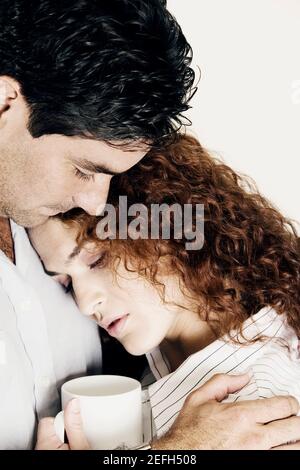 Seitenprofil einer jungen Frau, die eine Kaffeetasse hält Und schmiegte sich an einen jungen Mann Stockfoto