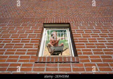 Ein bärtiger Mann, der in einer Schubkarre ein Bad nimmt, gesehen durch ein Backstein umgebenes Fenster. Zusammengesetztes Bild. Stockfoto