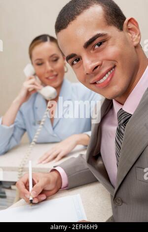 Porträt eines Geschäftsmannes, der lächelt und eine Dame an der Rezeption spricht Am Telefon hinter ihm Stockfoto
