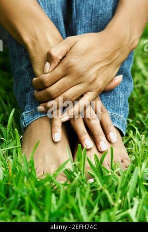 Niedrige Ansicht einer Frau, die auf dem Gras sitzt Mit ihren Knien umarmt Stockfoto