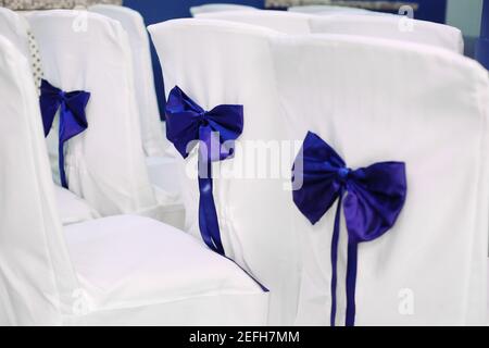 Stühle für Bankette im Restaurant vorbereitet. Bedeckt mit weißem Tuch und atlas blauen Bändern Schleifen Stockfoto