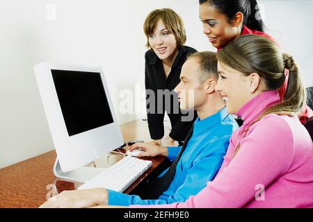 Nebenprofil eines Geschäftsmannes mit drei Geschäftsfrauen, die einen Desktop-PC verwenden Stockfoto