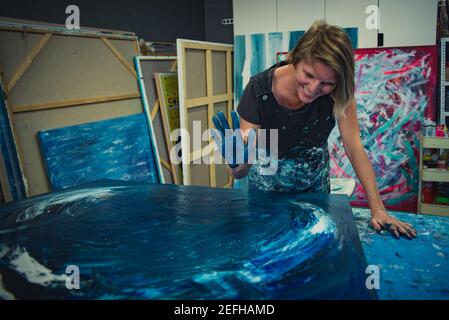 Die junge Frau malt mit Händen und Spachtel ein abstraktes Bild auf einem Arbeitstisch in ihrem Innenstudio. Konzentrieren Sie sich auf die Hand Stockfoto