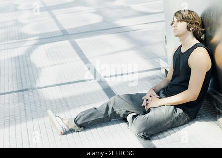 Seitenansicht eines jungen Mannes auf dem Boden sitzend Stockfoto