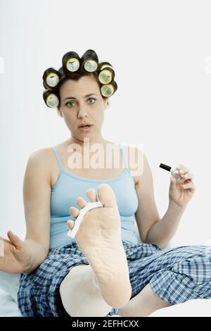 Porträt einer reifen Frau mit Lockenwicklern im Haar Halten Sie einen Nagellack Stockfoto