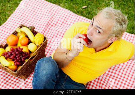 Porträt eines jungen Mannes, der sitzt und einen Apfel beißt Stockfoto