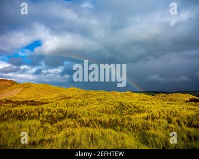 Sanddünen hinter dem Strand bei Morfa Dyffryn zwischen Barmouth und Harlech in Gwynedd an der Nordwestküste von Wales mit stürmischem Himmel und Regenbogen darüber. Stockfoto