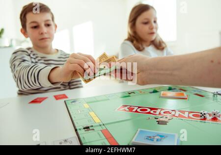 KIEL, DEUTSCHLAND - 14. Februar 2021: Hände mit Geld von glücklichen Kindern, die Spaß am Brettspiel in gemütlicher Familienzeit mit ihren Eltern haben Stockfoto