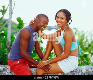 Porträt einer jungen Frau, die mit einem jungen Mann auf einem Felsen sitzt und lächelt, Bermuda Stockfoto