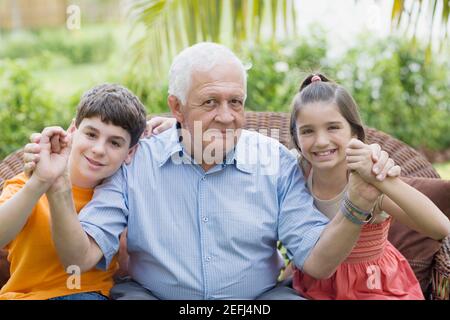 Porträt eines älteren Mannes, der seine grandchildrenÅ½s Hände hält und Lächelnd Stockfoto