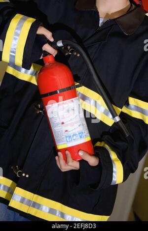 Mittlere Ansicht eines Jungen, der als Feuerwehrmann gekleidet ist Und einen Feuerlöscher halten Stockfoto