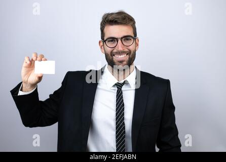 Junger Geschäftsmann in Anzug lächelnd und mit weißer Karte Stockfoto