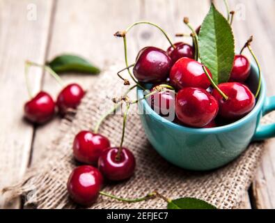 Kirschen in der schönen türkisfarbenen Tasse auf Holztisch, Makro-Hintergrund, Früchte, Beeren und Stockfoto