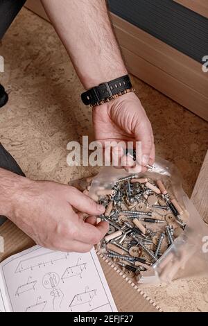 Kaukasische mans Hand Greifschraube. Mann, der neue Möbel zusammengebaut hat. Hausarbeit. Einzug. Nahaufnahme. Vertikale Aufnahme Stockfoto