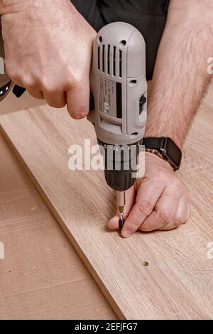 Kaukasische mans Hand hält einen elektrischen Schraubendreher. Mann montiert Möbel zu Hause. Hausarbeit. Nahaufnahme. Vertikale Aufnahme Stockfoto