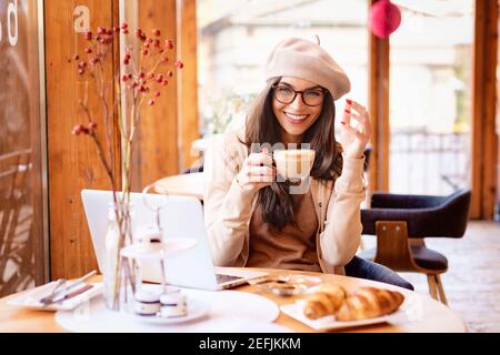 Aufnahme einer glücklichen Frau, die ihren Cappuccino trinkt, während sie am Kaffeetisch sitzt. Stockfoto