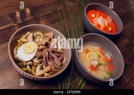 Satz serviert asiatische Suppen auf grauem Hintergrund der Ansicht von oben. Tom Yum Suppe, Aal Fischsuppe und Ramen Noodle Soup Stockfoto