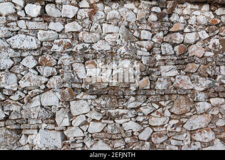 Alte Steinmauer, in einer verblassten weißen Farbe bemalt und mit Steinen und Schlamm gebaut Stockfoto