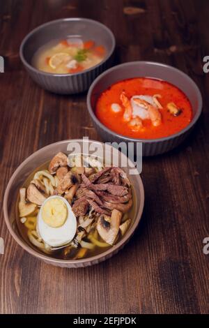 Satz serviert asiatische Suppen auf grauem Hintergrund der Ansicht von oben. Tom Yum Suppe, Aal Fischsuppe und Ramen Noodle Soup Stockfoto