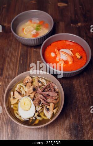 Satz serviert asiatische Suppen auf grauem Hintergrund der Ansicht von oben. Tom Yum Suppe, Aal Fischsuppe und Ramen Noodle Soup Stockfoto