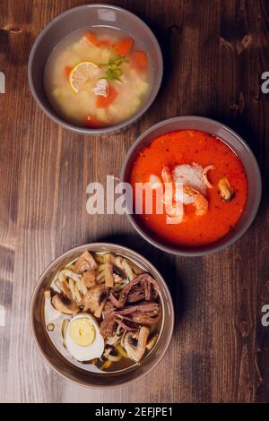 Satz serviert asiatische Suppen auf grauem Hintergrund der Ansicht von oben. Tom Yum Suppe, Aal Fischsuppe und Ramen Noodle Soup Stockfoto