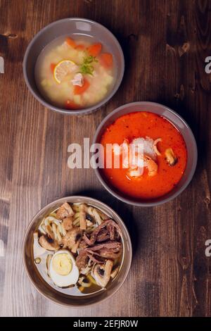 Satz serviert asiatische Suppen auf grauem Hintergrund der Ansicht von oben. Tom Yum Suppe, Aal Fischsuppe und Ramen Noodle Soup Stockfoto