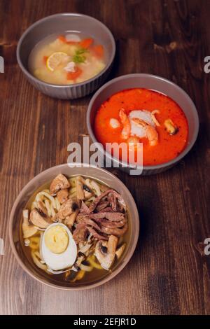 Satz serviert asiatische Suppen auf grauem Hintergrund der Ansicht von oben. Tom Yum Suppe, Aal Fischsuppe und Ramen Noodle Soup Stockfoto