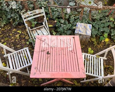 Nahaufnahme leerer Holztisch und Stühle mit getrockneten Blättern bedeckt Im Garten im Herbst Stockfoto
