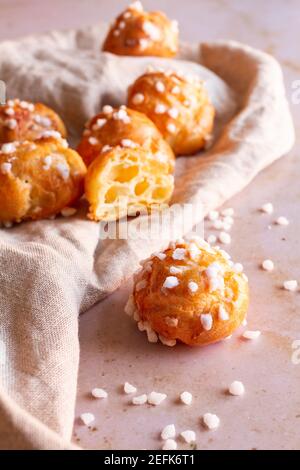 Frisch gebackene französische Chouquettes mit einem Schnitt in der Mitte auf einer beigefarbenen Leinenserviette. Stockfoto