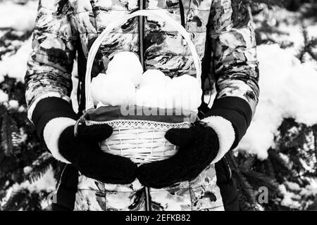 Ein Mädchen hält einen Korb mit Schneebällen in ihrem Schwarz Gestrickte Fäustlinge schwarz-weiß Foto Stockfoto