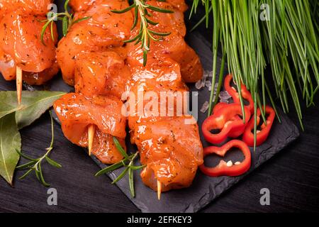 Hühnerstücke von Kebabs in einer roten Marinade mit Gewürzen auf einem dunklen kulinarischen Brett mariniert, auf einem Hintergrund mit Stücken von Pfeffer. Rohe Hähnchenstücke auf Stockfoto