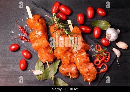 Hühnerstücke von Kebabs in einer roten Marinade mit Gewürzen auf einem dunklen kulinarischen Brett mariniert, auf einem Hintergrund mit Stücken von Pfeffer. Rohe Hähnchenstücke auf Stockfoto