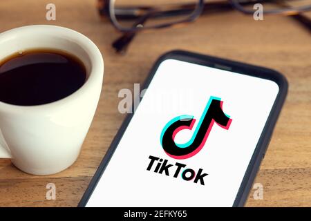 Galicia, Spanien; 15. februar 2021: TIK Tok Logo auf Smartphone-Bildschirm auf Schreibtisch mit Brille und Tasse Kaffee auf Holztisch Stockfoto