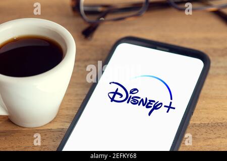 Galicia, Spanien; 15. februar 2021: Disney plus Logo auf Smart Phone Bildschirm auf Schreibtisch mit Brille und Tasse Kaffee auf Holztisch Stockfoto