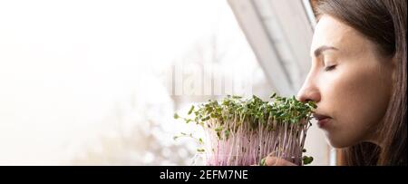 Frauen genießen frisch angebaute Mikrogrüns auf einem Schweller in der Nähe von sonnigen Fenster. Selbst angebaute gesunde Superfood Microgreens. Stockfoto